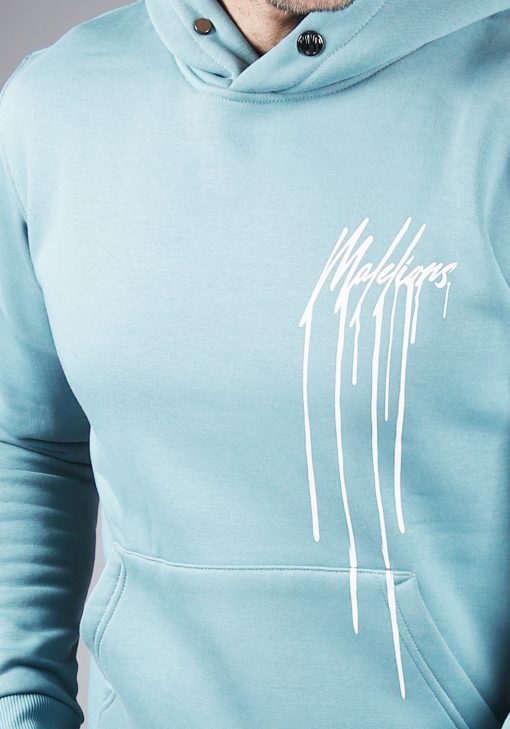Closeup van model gekleed in blauwe hoodie met het witte Malelions drip logo op de linkerborst.