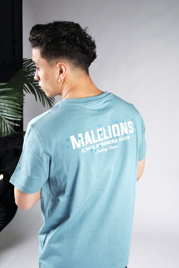 Schuin achteraanzicht van model gekleed in blauw Malelions t-shirt met witte tekst en blauwe verfspetters op de rug en linkerborst.