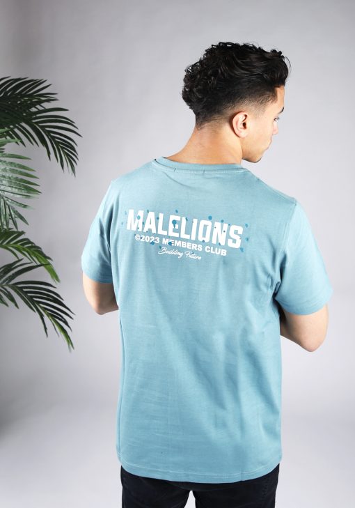 Achteraanzicht van model gekleed in blauw Malelions t-shirt met witte tekst en blauwe verfspetters op de rug en linkerborst.