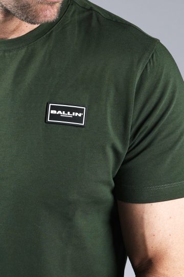 Close up vooraanzicht van model gekleed in donkergroen t-shirt met een kleine zwarte badge op de linkerborst met het witte Ballin logo.
