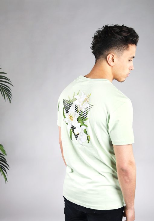 Achteraanzicht van model gekleed in lichtgroen t-shirt met driekhoek bloemenprint op de rug, en het kleine zwarte logo op de borst.