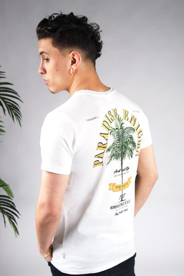 Schuin achteraanzicht van model gekleed in witte paradise tee met een print van een palmboom omringd met tekst op de rug en een klein logo op de voorkant.