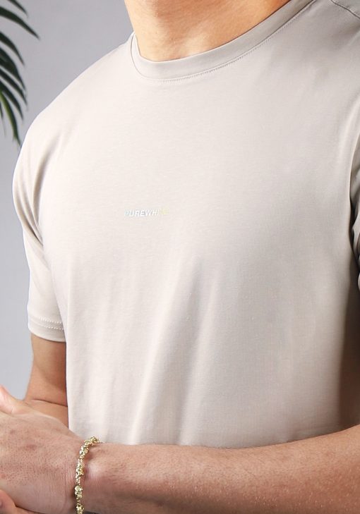 Close up vooraanzicht van model gekleed in zandkleurig t-shirt met gestreepte driehoek print op de rug en het kleine logo op de borst. De prints hebben een faded kleur van mintgroen, naar wit, tot geel.