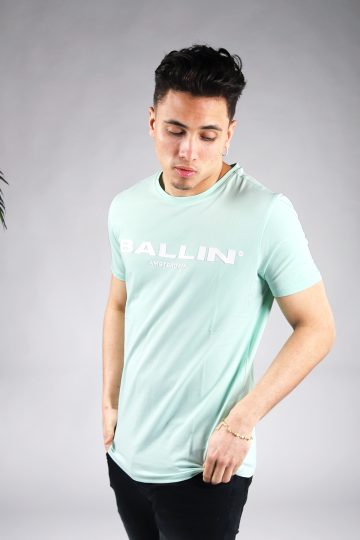 Vooraanzicht van model gekleed in mintgroen t-shirt met de witte tekst Ballin Amsterdam op de voorkant. Het model heeft zijn handen bij zijn broekzakken.