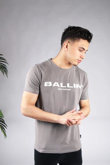 Vooraanzicht van model gekleed in grijs t-shirt met de witte tekst Ballin Amsterdam op de voorkant. Het model heeft zijn handen voor zich.