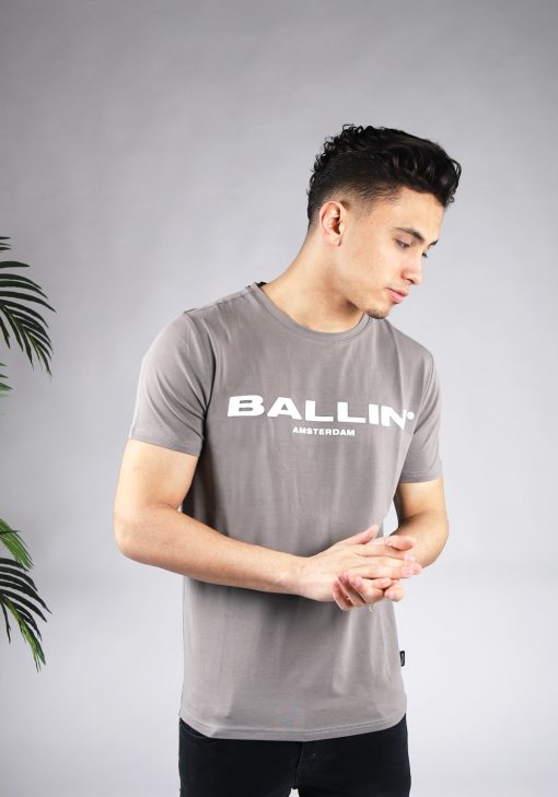 Vooraanzicht van model gekleed in grijs t-shirt met de witte tekst Ballin Amsterdam op de voorkant. Het model heeft zijn handen voor zich.