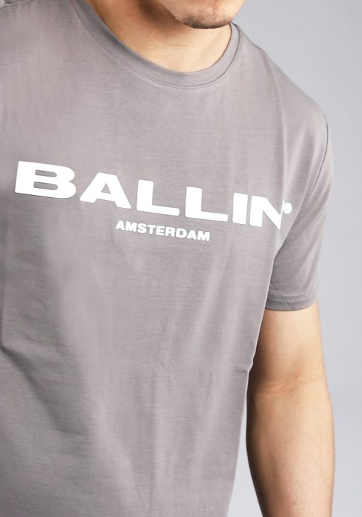 Close up vooraanzicht van model gekleed in grijs t-shirt met de witte tekst Ballin Amsterdam op de voorkant.