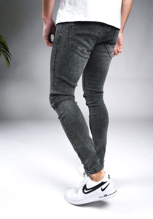 Achteraanzicht grijze heren skinny jeans met damaged look, gemaakt van stretch stof. Voorzien van vier zakken, knoopsluiting en riemlussen. Gecombineerd met wit T-shirt en witte sneakers.