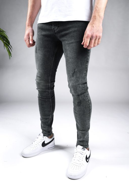 Linker zijaanzicht grijze heren skinny jeans met damaged look, gemaakt van stretch stof. Voorzien van vier zakken, knoopsluiting en riemlussen. Gecombineerd met wit T-shirt en witte sneakers.