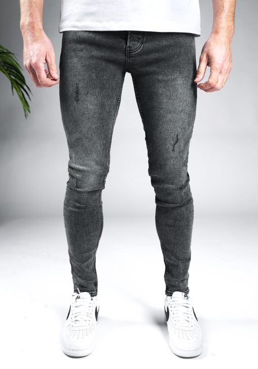 Voorkant grijze heren skinny jeans met damaged look, gemaakt van stretch stof. Voorzien van vier zakken, knoopsluiting en riemlussen. Gecombineerd met wit T-shirt en witte sneakers.