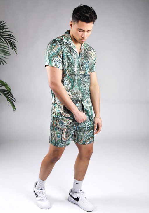Schuin vooraanzicht van model gekleed in jungle set met drukke gekleurde print. De set bestaat uit shorts en een blouse met korte mouwen.