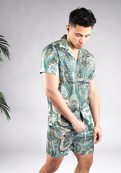 Schuin vooraanzicht van model gekleed in jungle set met drukke gekleurde print. De set bestaat uit shorts en een blouse met korte mouwen.