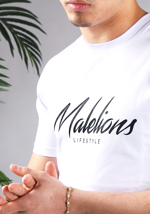Close up vooraanzicht van model gekleed in wit Malelions t-shirt met een zwart logo en zwarte tekst op de voorkant.