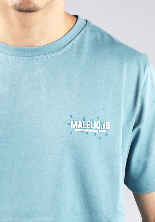 Close up vooraanzicht van model gekleed in blauw Malelions t-shirt met witte tekst en blauwe verfspetters op de rug en linkerborst.