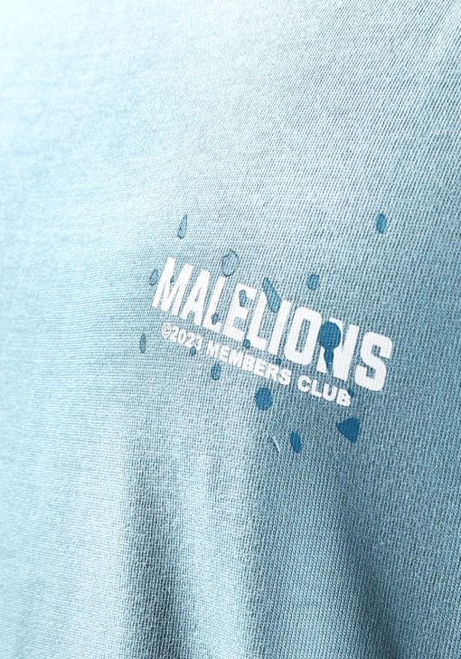 Close up borst van model gekleed in blauw Malelions t-shirt met witte tekst en blauwe verfspetters op de rug en linkerborst.
