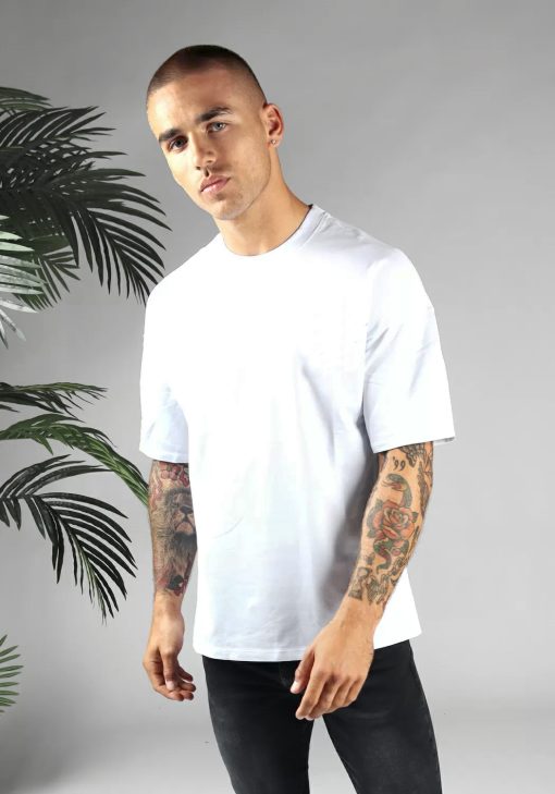Vooraanzicht van heren T-shirt in witte kleur, met ronde hals en oversized pasvorm. Het model draagt een donkere jeans en heeft zijn armen langs zijn lichaam.