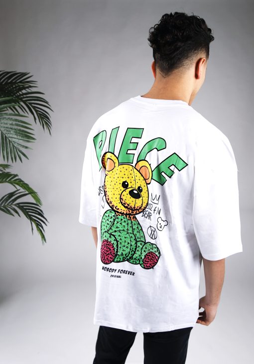Achteraanzicht van een heren T-shirt in witte kleur en een super oversized pasvorm. Het T-shirt is voorzien van groene tekst en een beer op de achterkant. Het model laat zijn armen langs zijn lichaam hangen en draagt een donkere jeans.