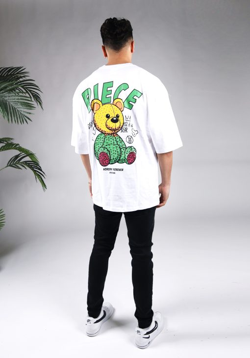 Achteraanzicht van een heren T-shirt in witte kleur en een super oversized pasvorm. Het T-shirt is voorzien van groene tekst en een beer op de achterkant. Het model laat zijn armen langs zijn lichaam hangen, draagt een donkere jeans en witte sneakers.