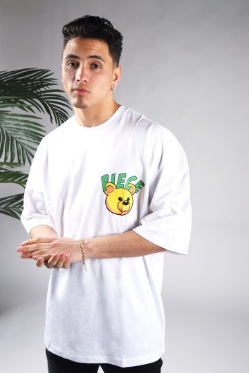 Vooraanzicht van een heren T-shirt in witte kleur en een super oversized pasvorm. Het T-shirt is voorzien van groene tekst en het hoofd van een beer op de linkerborst. Het model wrijft in zijn handen en draagt een donkere jeans.
