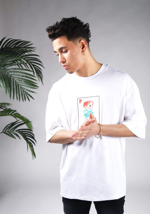 Vooraanzicht van een heren T-shirt in witte kleur en een super oversized pasvorm. Het T-shirt is voorzien van een pixelart speelkaart met daarop een pixelart karakter op de voorkant. Het model wrijft in zijn handen en draagt een donkere jeans.
