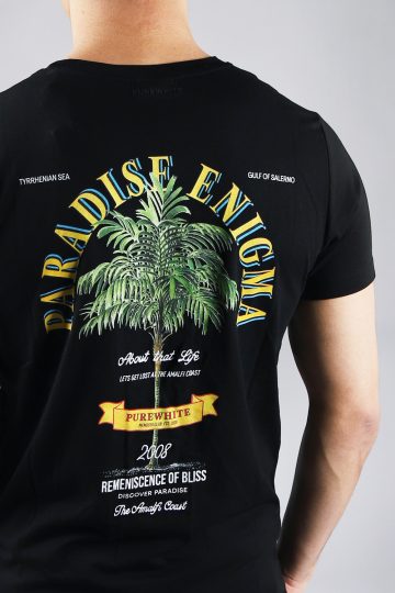 Close up achteraanzicht van model gekleed in zwarte paradise tee met een print van een palmboom omringd met tekst op de rug en een klein logo op de voorkant.
