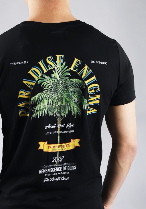 Close up achteraanzicht van model gekleed in zwarte paradise tee met een print van een palmboom omringd met tekst op de rug en een klein logo op de voorkant.