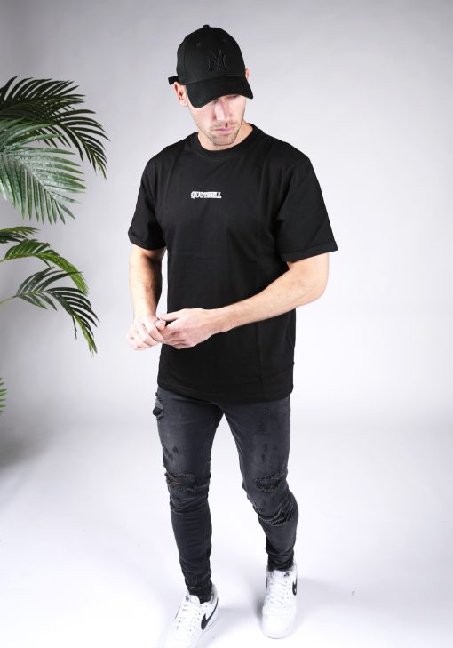 Vooraanzicht van heren T-shirt in zwarte kleur, met een ronde hals en een relaxed fit pasvorm. Het T-shirt is voorzien van het QUOTRELL-logo in het wit op de borst. Het T-shirt wordt gecombineerd met een donkere jeans en witte sneakers.
