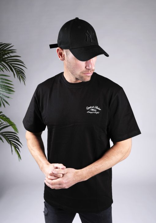 Vooraanzicht van model gekleed in een zwart T-shirt met witte tekst op de linkerborst.