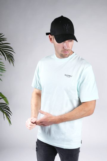 Linker vooraanzicht van model gekleed in blauw heren T-shirt met een ronde hals en een relaxed fit pasvorm. Het T-shirt is voorzien van het QUOTRELL logo op de linkerborst.