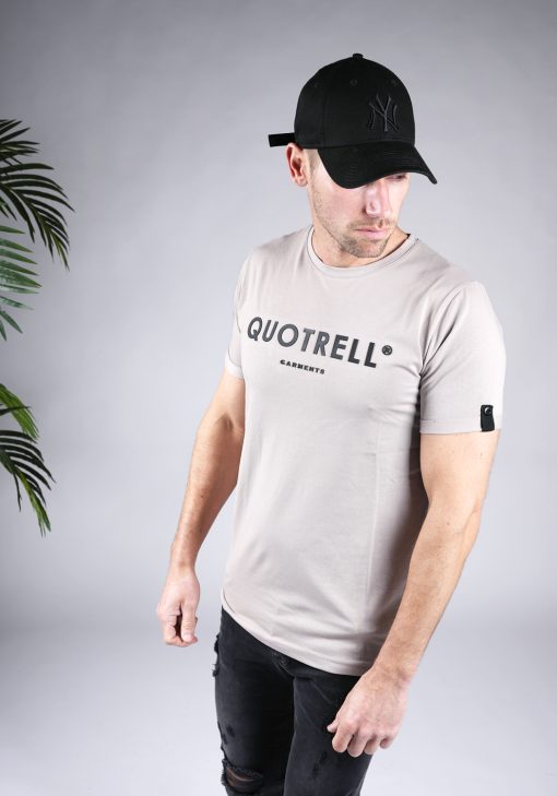 Linker vooraanzicht van heren T-shirt in taupe kleur, met ronde hals en een slim fit pasvorm. Het T-shirt is voorzien van het QUOTRELL-logo in zwarte kleur op de borst. Het model combineert het T-shirt met een donkere jeans.