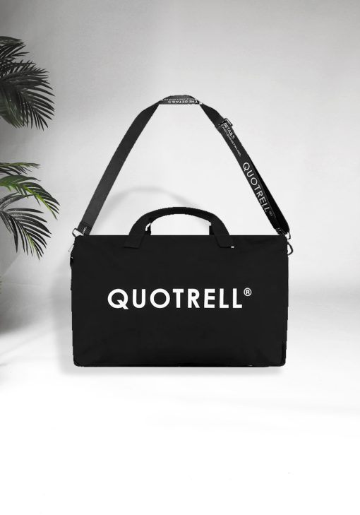 Vooraanzicht van grote zwarte Quotrell tote bag. De tas is voorzien van het grote witte Quotrell logo op de voorkant en heeft een schouderhengsel met daarop ook verschillende teksten. De tas heeft ook twee handvaten naast het schouderhengsel.