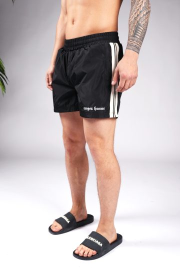 Linker zijaanzicht van model gekleed in zwarte Croyez Vice swimshorts met het witte Croyez logo op de linkerbeen en zwarte witte verticale lijnen aan de zijkant.