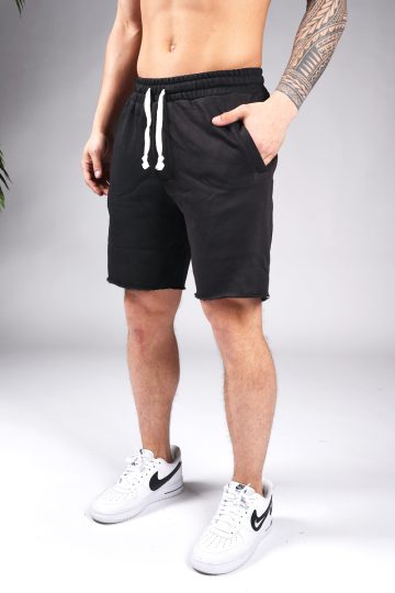 Linker vooraanzicht van model gekleed in zwarte jogger shorts met witte touwtjes. Het model heeft een hand in zijn zak en draagt witte sneakers.