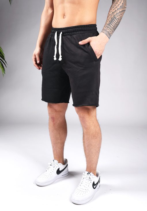 Linker vooraanzicht van model gekleed in zwarte jogger shorts met witte touwtjes. Het model heeft een hand in zijn zak en draagt witte sneakers.