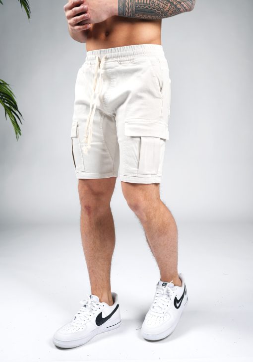 Linker vooraanzicht van model gekleed in zandkleurige cargo shorts in combinatie met witte sneakers. Het model heeft zijn handen voor zich.