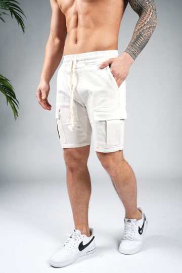 Linker vooraanzicht van model gekleed in zandkleurige cargo shorts in combinatie met witte sneakers. Het model heeft een van zijn handen in zijn zakken.