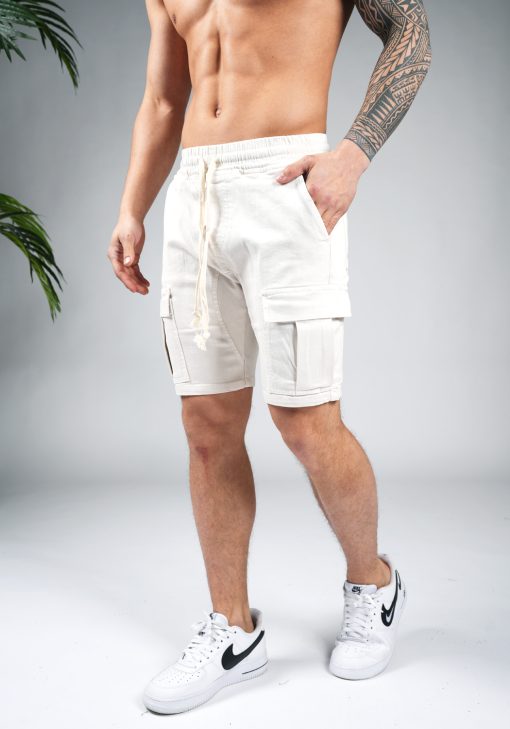Linker vooraanzicht van model gekleed in zandkleurige cargo shorts in combinatie met witte sneakers. Het model heeft een van zijn handen in zijn zakken.