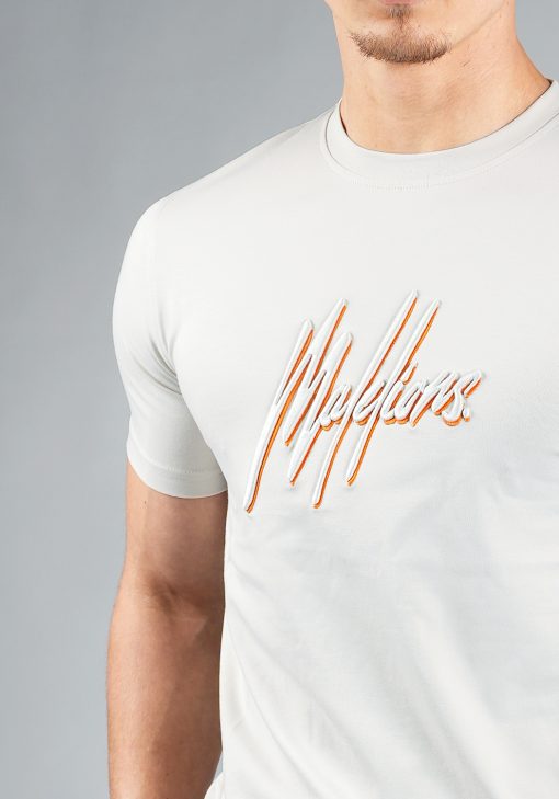Close up shirt van model gekleed in lichtgrijze Malelions set. De set bestaat uit een shirt met het dubbelkleurige geborduurde Malelions logo in het grijs en oranje, en de shorts met hetzelfde logo op de been.