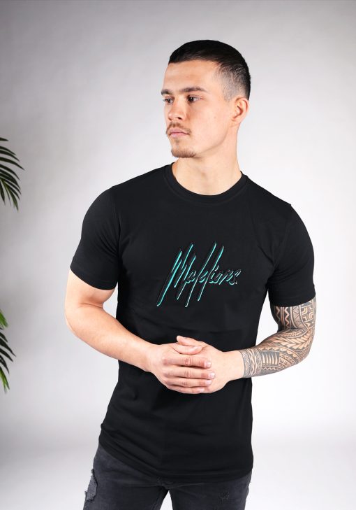 Vooraanzicht van model gekleed in zwart Malelions t-shirt met het dubbel geborduurde logo in de kleuren turquoise en zwart op de borst. Het model heeft zijn handen voor zich en kijkt naar rechts.