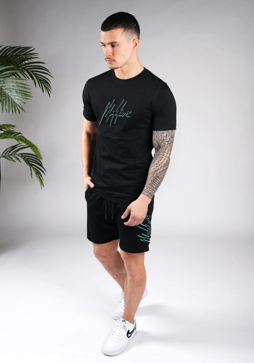 Full body vooraanzicht van model gekleed in zwarte Malelions set. De set bestaat uit een zwart t-shirt met het zwart-turquoise Malelions logo op de borst, en de jogger shorts met het grote logo verticaal op de been.