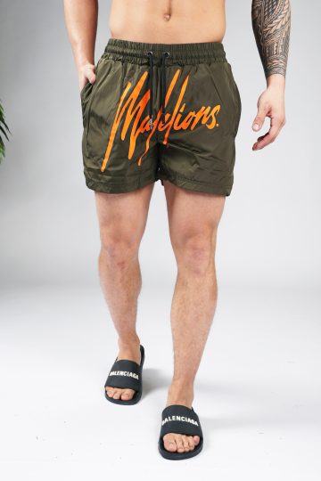 Vooraanzicht van model gekleed in legergroene swimshorts met het grote oranje Malelions logo op de voorkant.