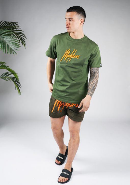 Vooraanzicht van model gekleed in legergroene swimshorts met het grote oranje Malelions logo op de voorkant in combinatie met het groene shirt.