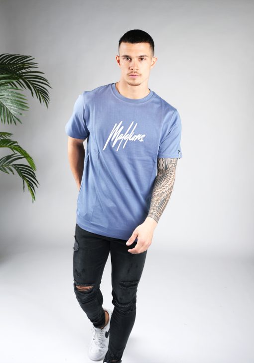 Vooraanzicht van model gekleed in een blauw gekleurd heren T-shirt. Het T-shirt is voorzien van het MALELIONS-logo op de borst in witte kleur en een relaxed fit pasvorm. Het T-shirt wordt gecombineerd met een donkere jeans en witte sneakers.