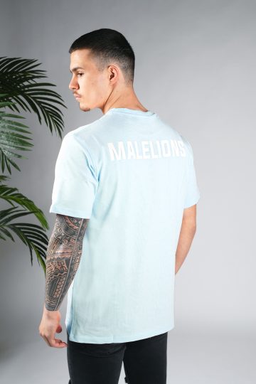 Schuin achteraanzicht van model gekleed in een lichtblauw gekleurd heren T-shirt. Het T-shirt is voorzien van het MALELIONS-logo op de borst in witte kleur op de achterkant.