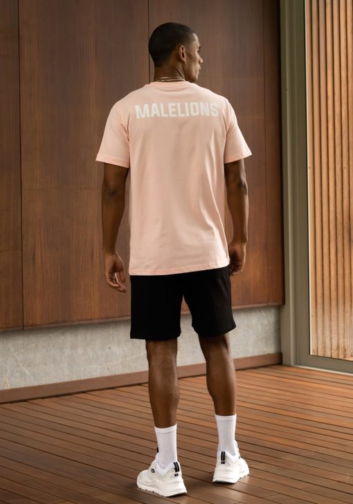 Totaal achteraanzicht van model gekleed in een lichtroze gekleurd heren T-shirt. Het T-shirt is voorzien van het MALELIONS-logo op de borst in witte kleur op de achterkant.