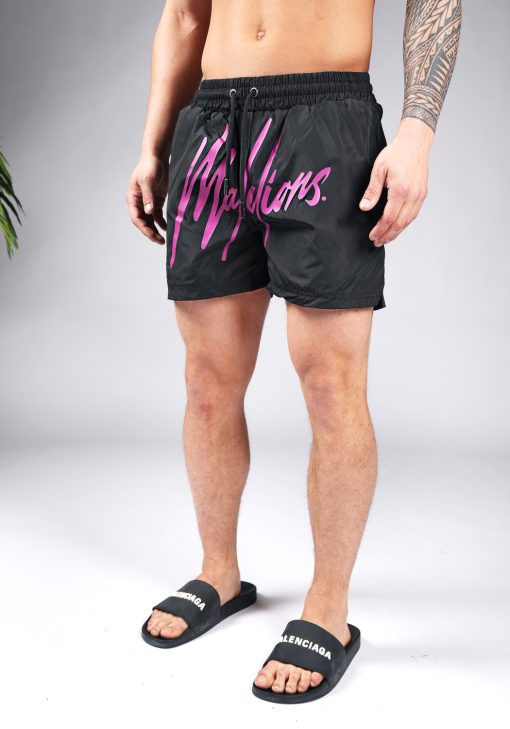 Vooraanzicht van model gekleed in zwarte swimshorts met het grote paarse Malelions logo op de voorkant.
