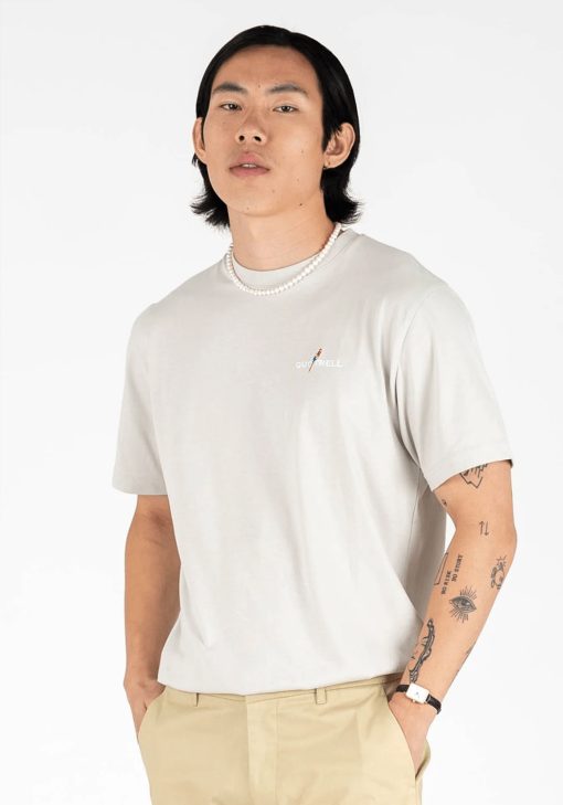 Vooraanzicht van model gekleed in een heren T-shirt in lichtgrijze kleur, met een ronde hals en een relaxed fit pasvorm. Het T-shirt is voorzien van het QUOTRELL-logo en een papegaai op de linkerborst.