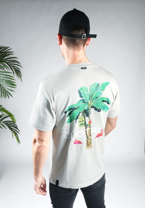 Schuin achteraanzicht van model gekleed in een heren T-shirt in lichtgrijze kleur, met een ronde hals en een relaxed fit pasvorm. Het T-shirt is voorzien van palmboom print, flamingo's en lichte tekst op de achterkant.
