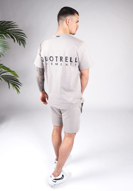 Achteraanzicht van model gekleed in taupe kleurige Quotrell set. De set bestaat uit jog shorts en een t-shirt. In het midden van de borst, de rug en op het linker bovenbeen staat de tekst Quotrell.