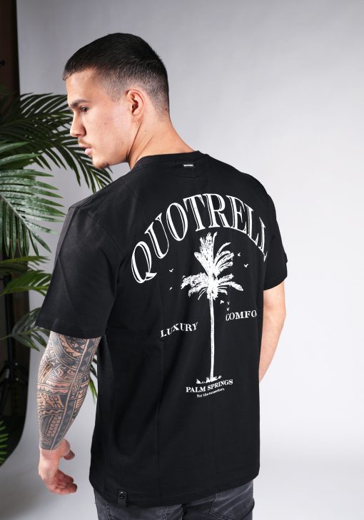 Achteraanzicht van model gekleed in een heren T-shirt in zwarte kleur, met een ronde hals en een relaxed fit pasvorm. Het T-shirt is voorzien van palmboom print en de merknaam in witte kleur.